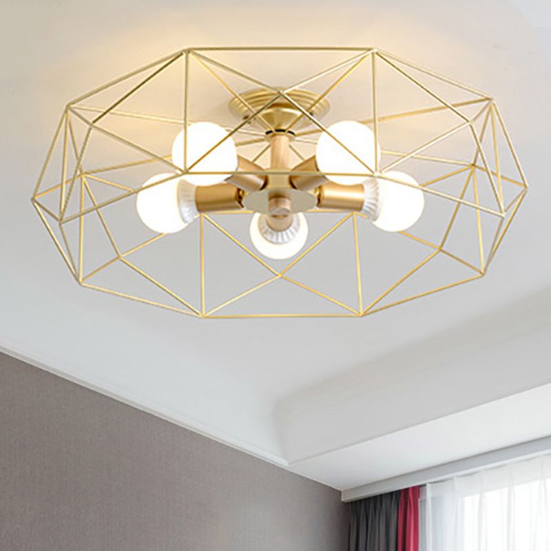 Gold five-light Cooley lantern with lit bulbs and pale wood-toned stem, near a grey wall, red drape and sheer window curtain.