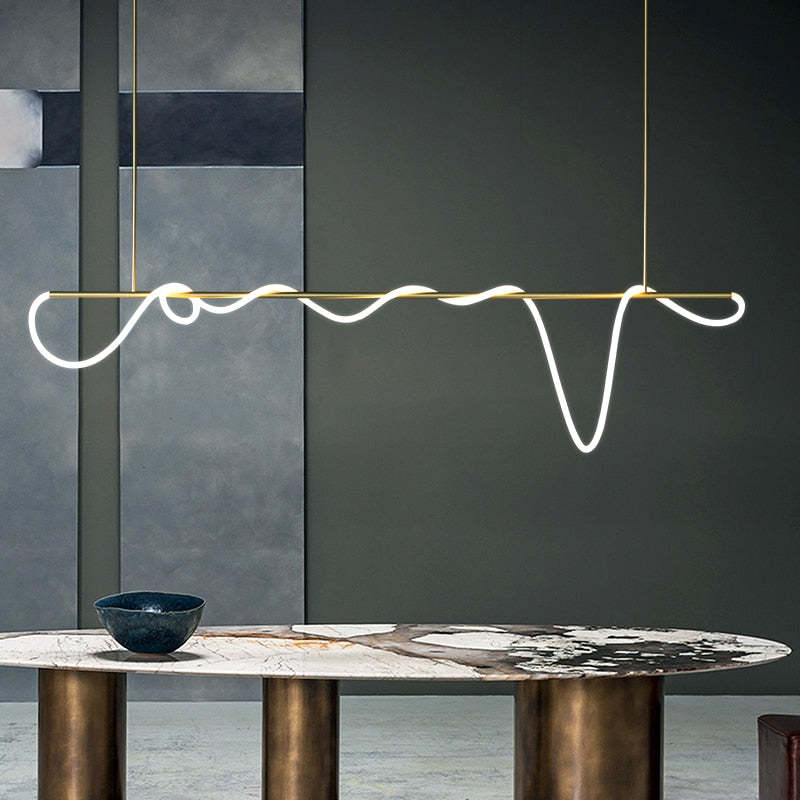 Gold Louise linear light with luminous loops above a veined oval table with gold-tone cylindrical legs and a dark bowl.