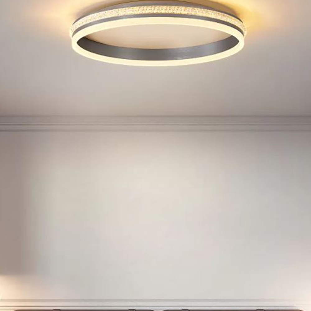 Cropped view of a lit Quinn ring on a pale ceiling, showing its open centre and brushed inner band above wall moulding.