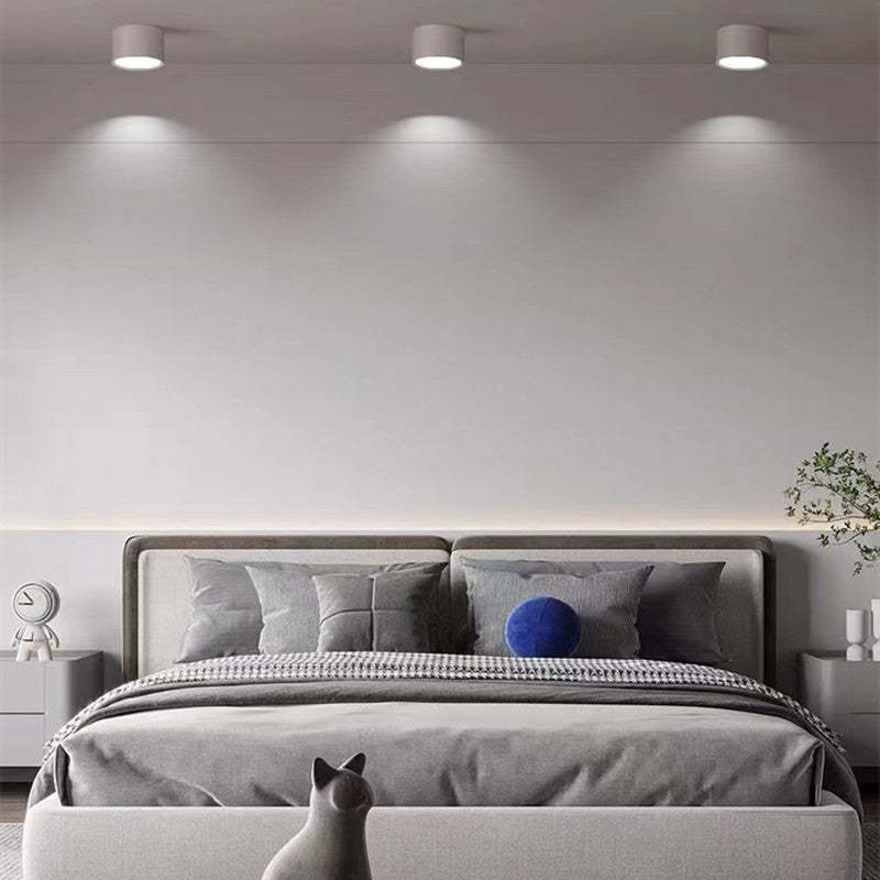 Three white Morandi cylinders above a gray bedroom with padded headboard, blue round cushion, clock and plants.