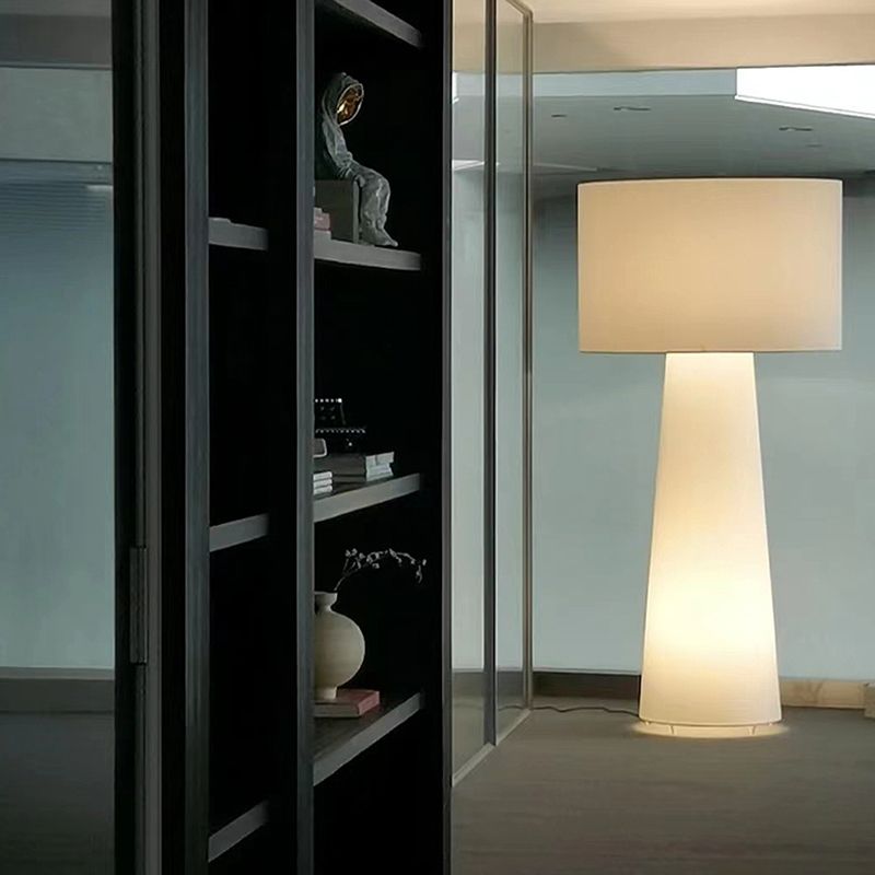 Single glowing floor lamp by a glass door and dark shelves with books and vases, cable running along the floor