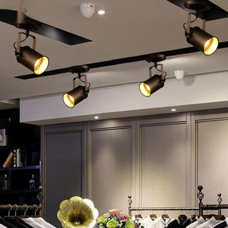 Separate single-head Alessio fixtures above clothing rails, grey wall panels, flowers and a gramophone horn in a display.