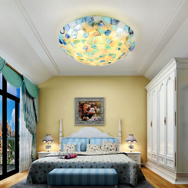 Blue-toned Morandi shell-mosaic ceiling light above a bed in a blue-and-white bedroom.