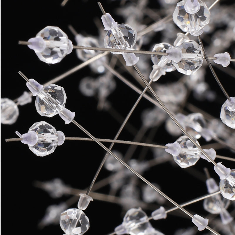 Clear faceted crystal beads on crossing fine metal stems with small pale collars, shown close-up against a dark background.