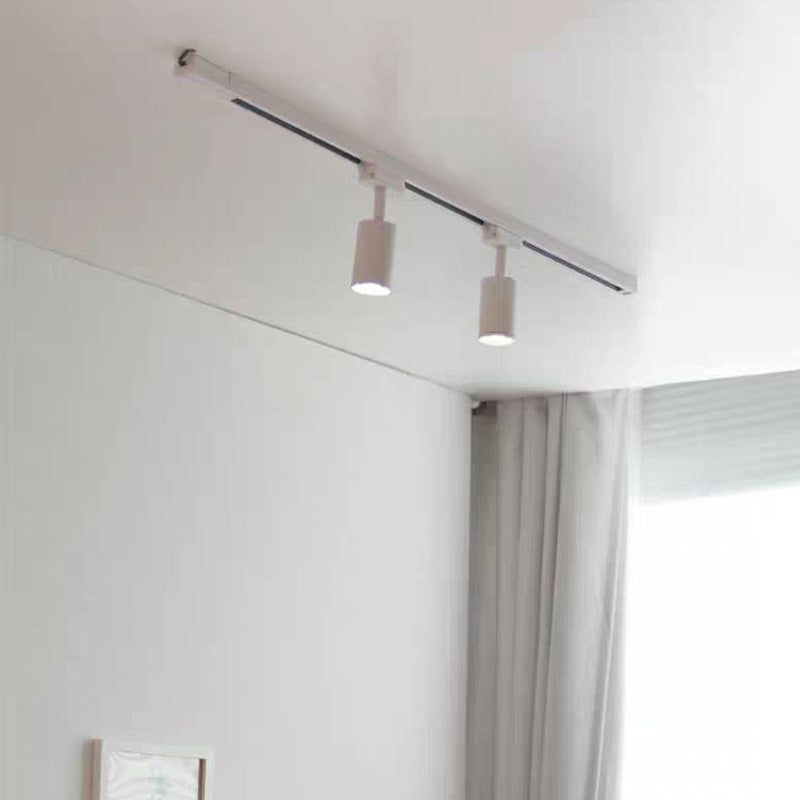 White Freja two-head ceiling track beside grey curtains and a framed wall image, with both cylindrical heads pointing downward.