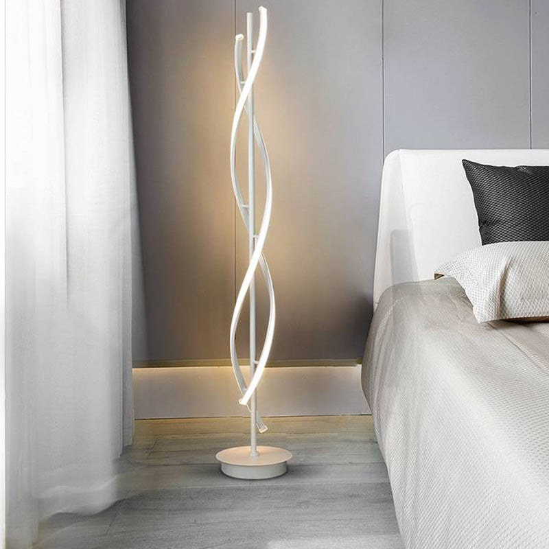 White curved-strip Louise floor lamp beside a gray bed and sheer curtain