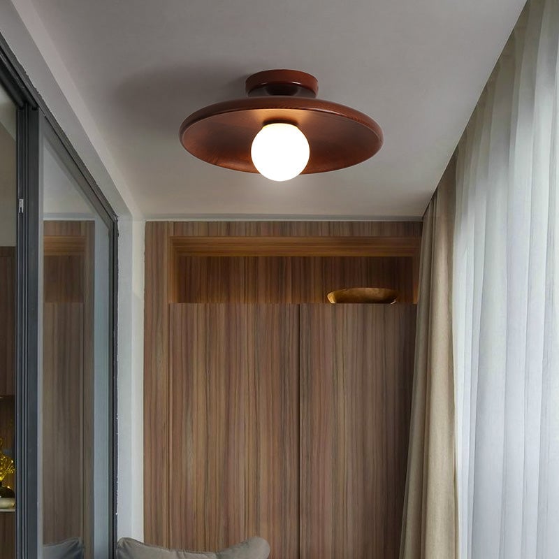 Dark walnut-tone Carins disc ceiling light and white globe above a wood cabinet, beside glass doors, sheer curtains and a grey cushion.