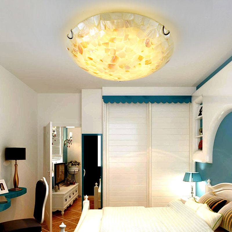 Pale Morandi shell-mosaic light illuminating a bedroom ceiling.