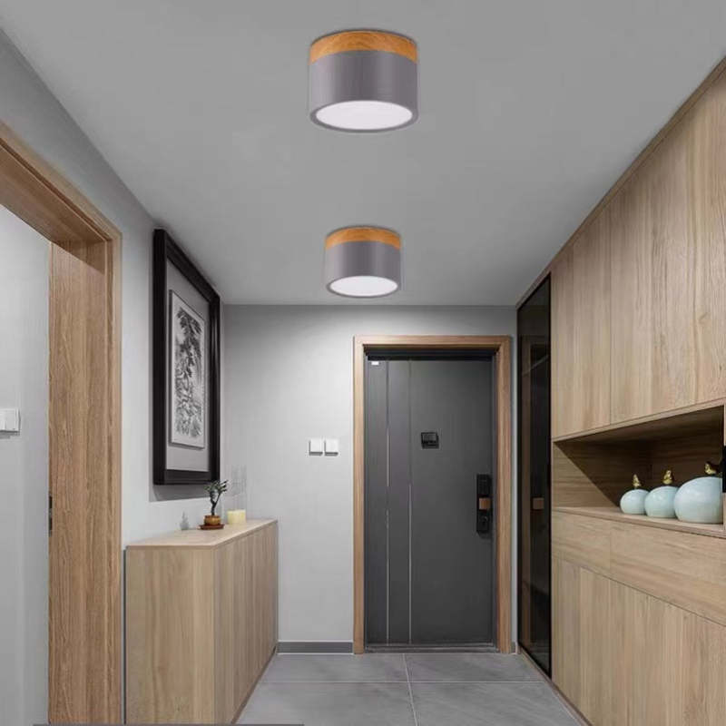 Two gray Morandi cylinders in an entry with wood cupboards, pale-green vases, gray door and framed art.