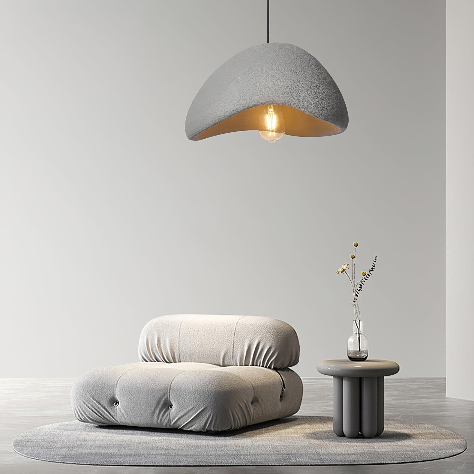 Gray textured cloud pendant with an exposed glowing bulb above a low gray chair and a small table with vase