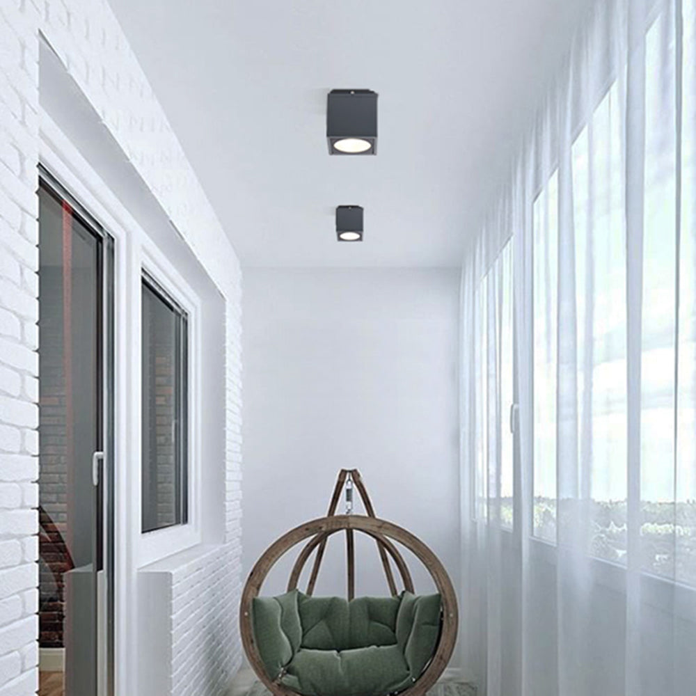 Black Orr cubes on a glazed balcony ceiling near white brick, windows and a circular hanging chair with green cushions.