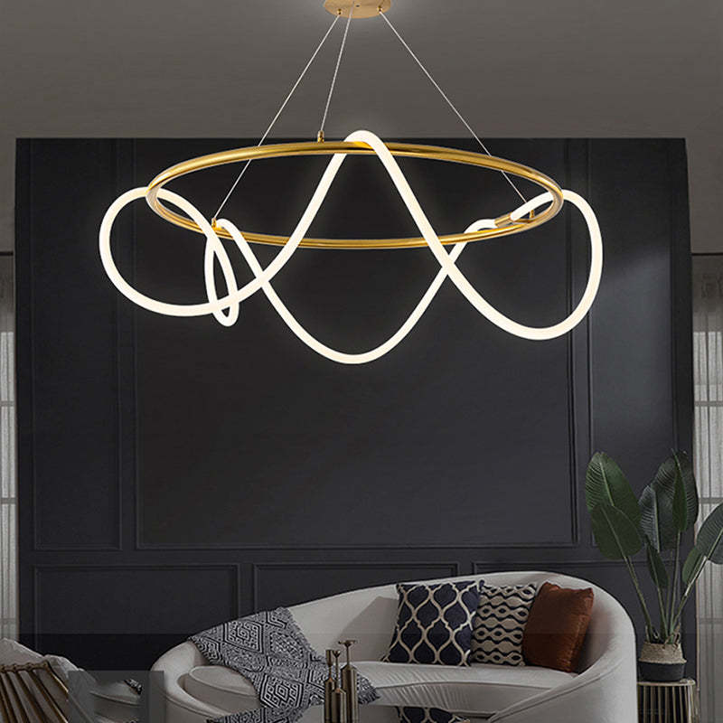 Gold Louise ring and luminous loops above a curved white sofa, patterned pillows and books, beside a plant and candleholders.