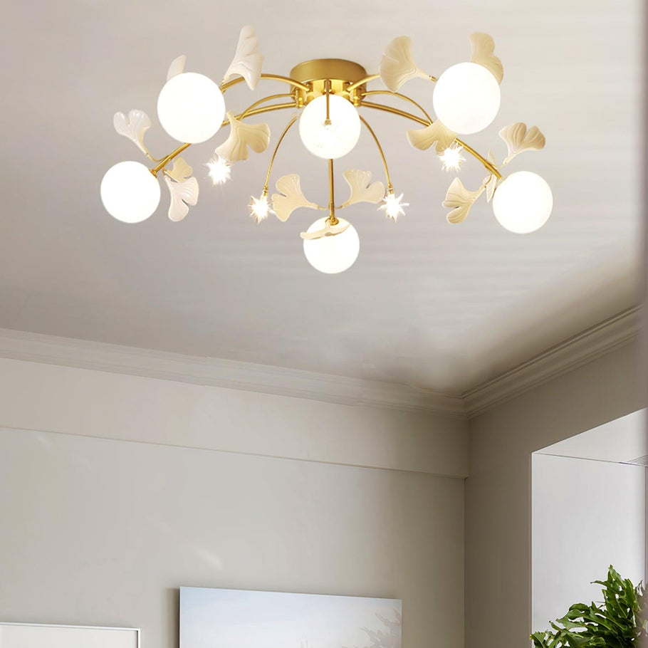 Olivia 5+6 Heads with lit white globes, small stars and pale ginkgo leaves at a cream ceiling, near a doorway and green foliage.