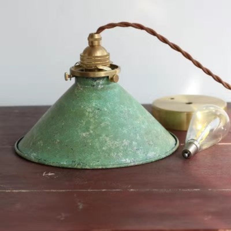Green Alessio cone on a tabletop beside a loose clear bulb and round gold-coloured canopy, with brown cord and top fittings.