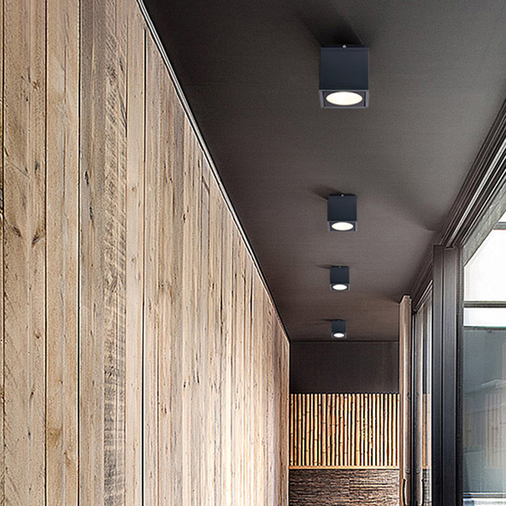 Black Orr cubes along a covered corridor beside a vertical timber wall and glazing, with a slat screen at the far end.