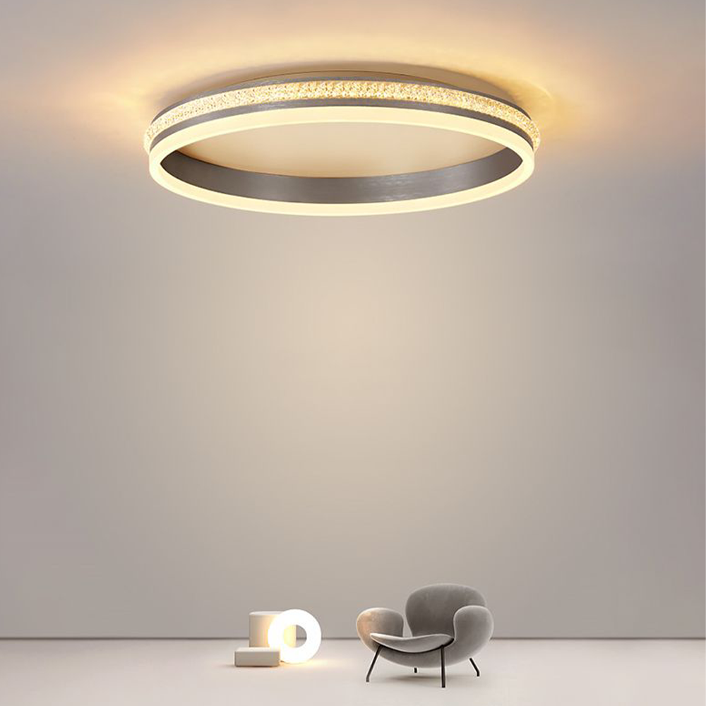 Large lit Quinn ring above a staged gray lounge chair and separate small glowing circular object against a pale background.
