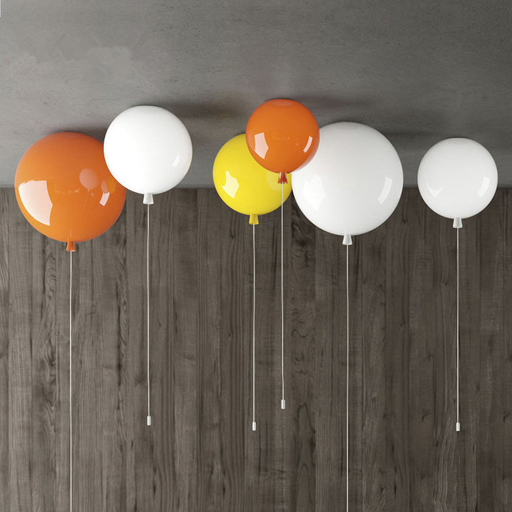 Separate glossy orange, white and yellow balloon fittings at a grey ceiling beside a wood-grain wall, with long fine strings.