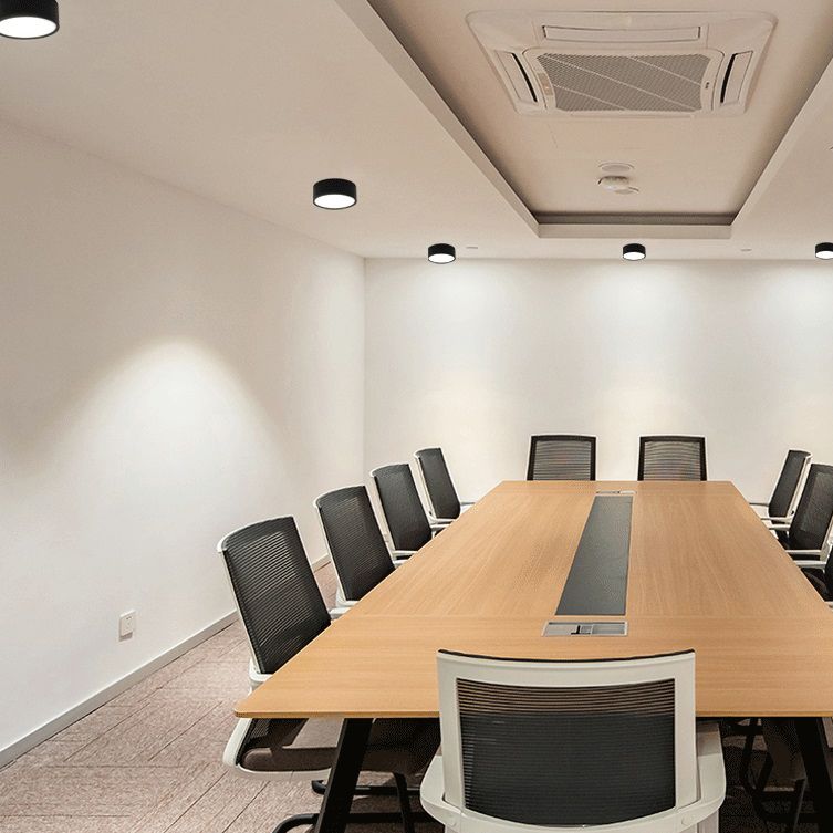 Black Quinn ceiling lights above a long wooden conference table with mesh chairs and a recessed ceiling cassette.