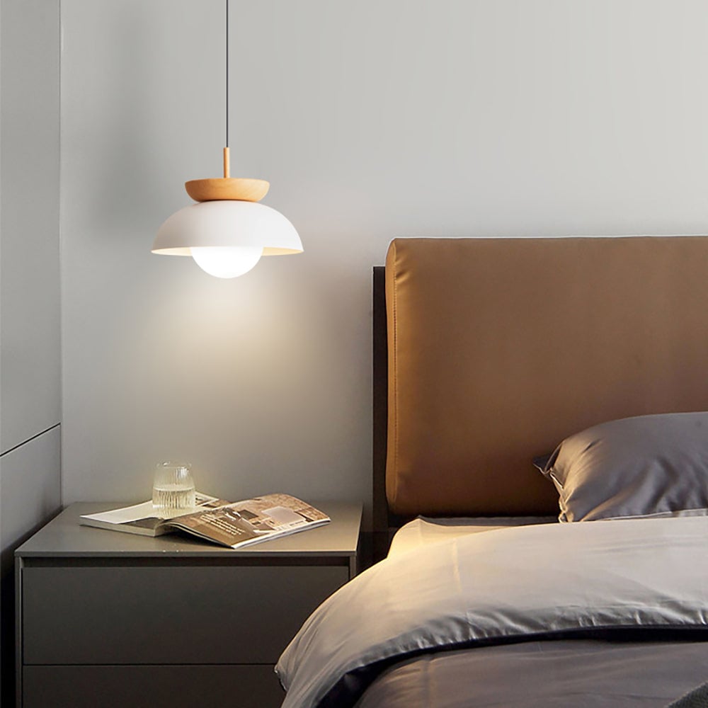 Lit white Ozawa pendant beside a tan upholstered headboard, above bedside drawers with an open magazine and glass
