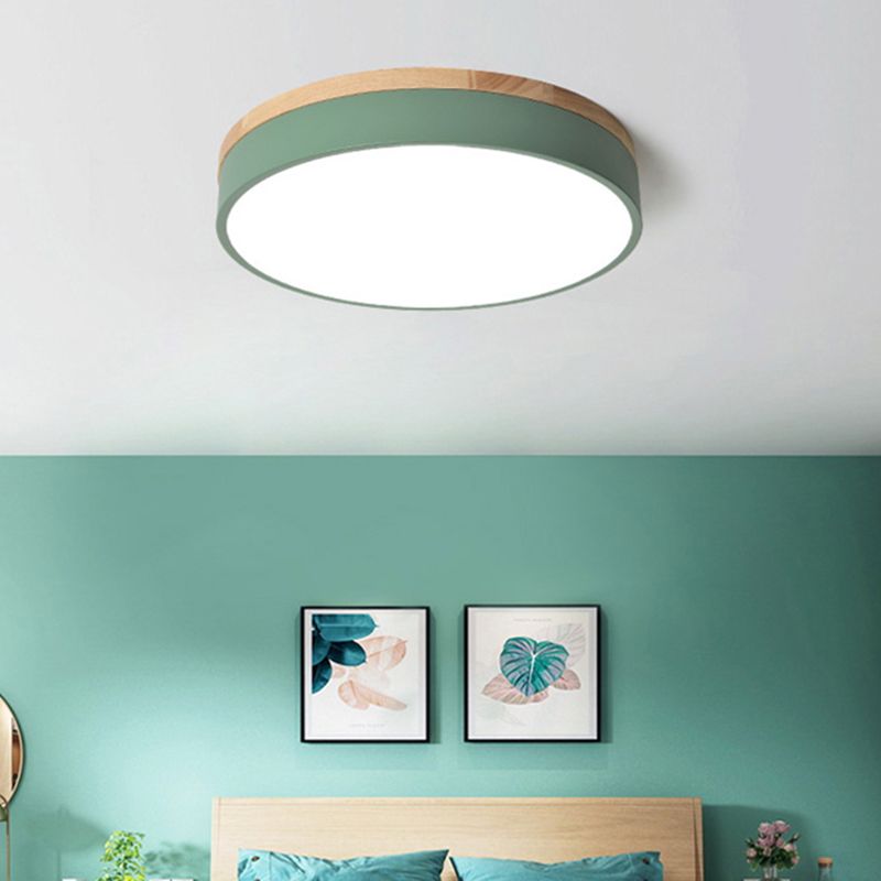 Green Morandi ceiling light above a green bedroom wall, wooden headboard, green pillows and two botanical prints.