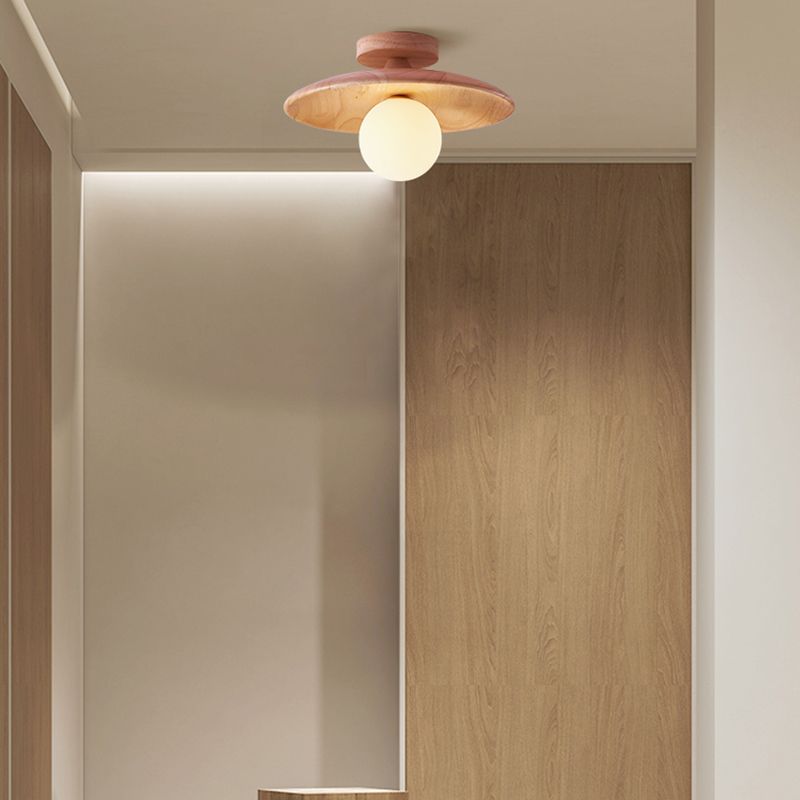 Light wood-tone Carins disc and round canopy with a warm-looking white globe above a large mirror, wood wall panel and partial counter.