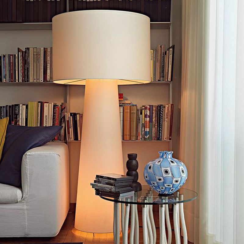 Glowing pale floor lamp beside a white sofa and a round glass table with a blue vase, bookshelves behind