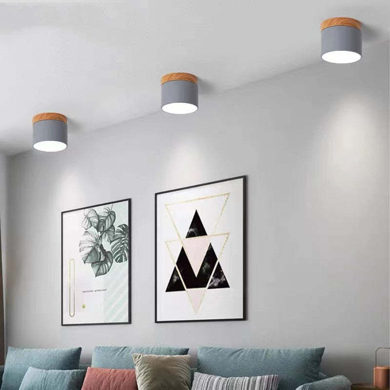 Three gray Morandi cylinders above leafy and geometric framed art, a blue-gray sofa and assorted cushions.