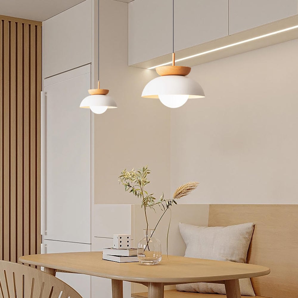 Two lit white dome pendants above a wooden table and upholstered banquette beside cupboards and timber slats
