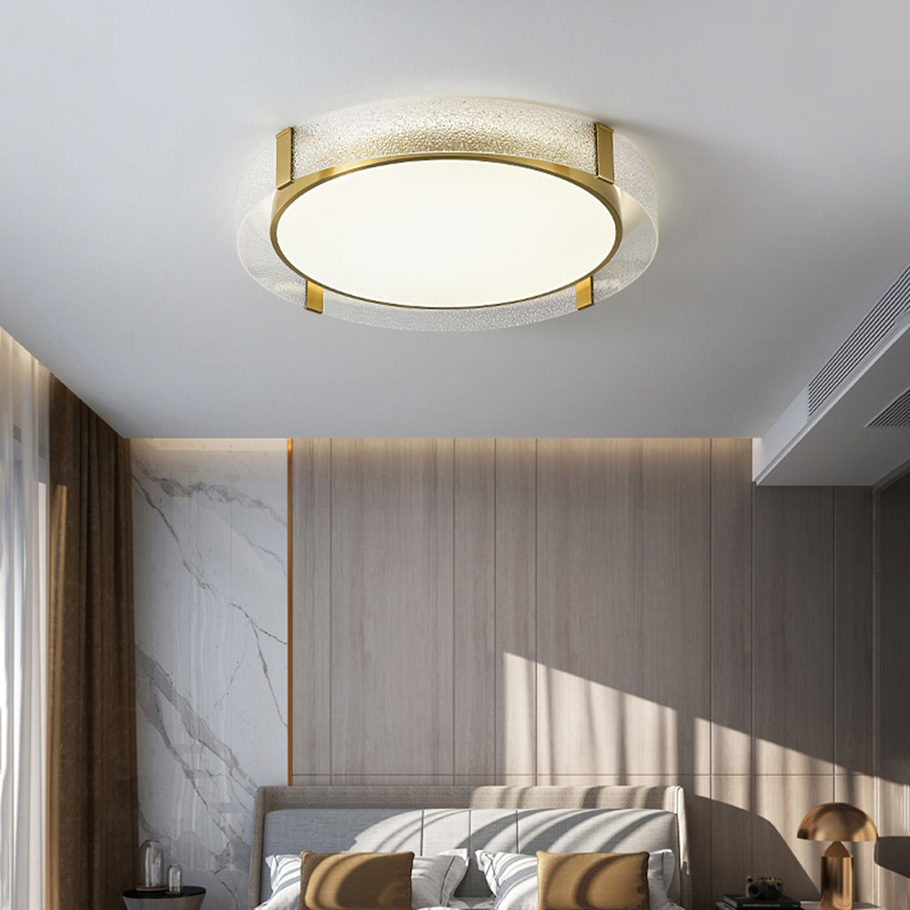 Quinn above a grey upholstered bed with tan cushions, wood-panel wall, pale veined side panel and separate gold-tone dome bedside lamp.