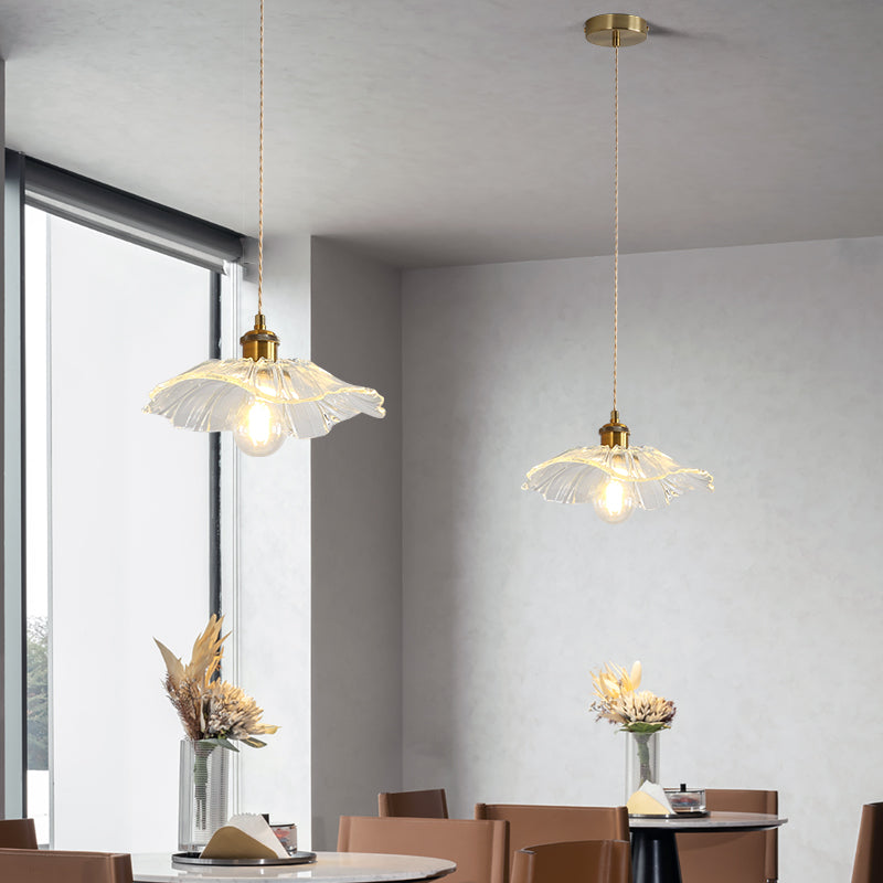 Two clear Carins pendant lights on cords above round black cafe tables with wooden chairs, vases and a large window.