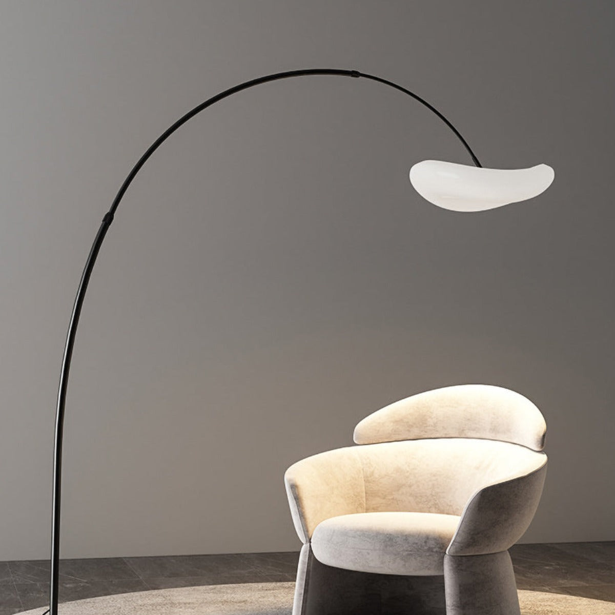 Black Minori arc floor lamp extending over a pale upholstered chair.