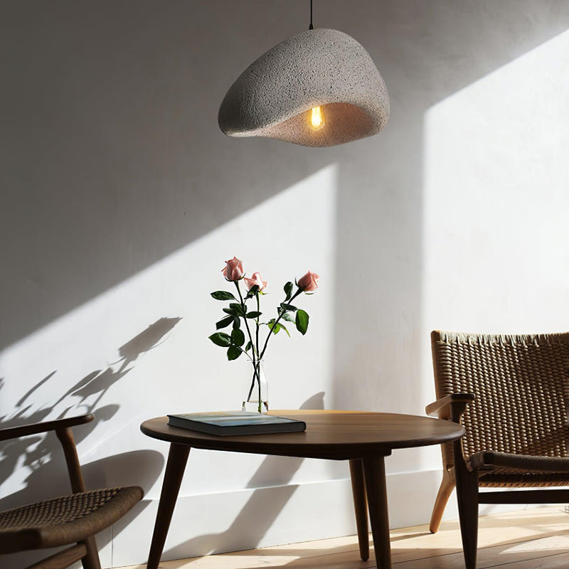 Gray speckled pendant above a round wooden table with roses and a book between woven chairs in sunlight