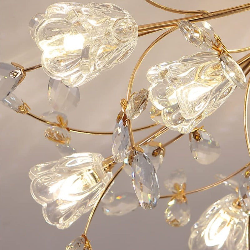 Close-up of glowing Lili clear sculpted flower shades among gold-tone branches and faceted leaf ornaments.