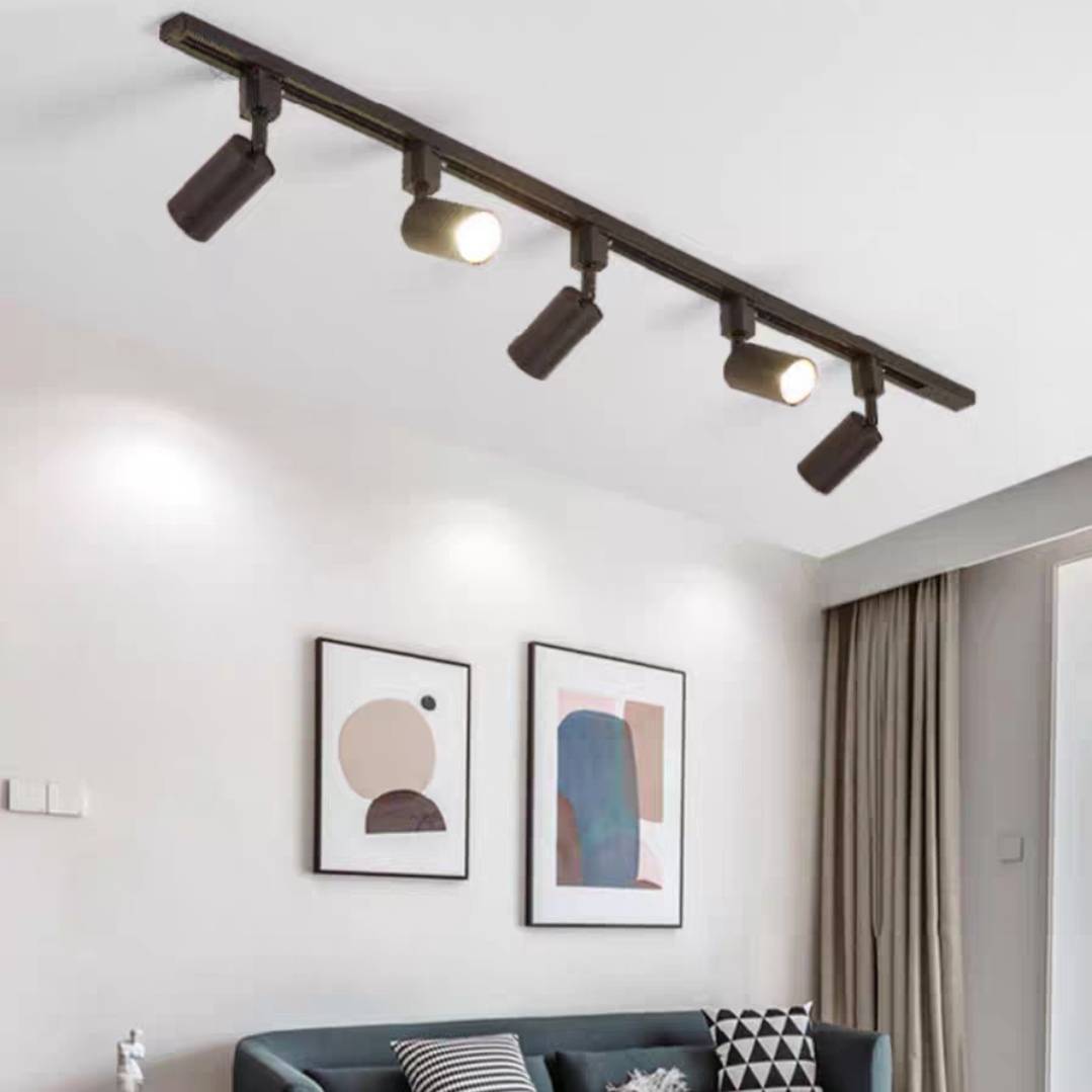 Black Freja five-head track above a teal sofa, striped and geometric cushions, abstract wall prints and grey curtains.