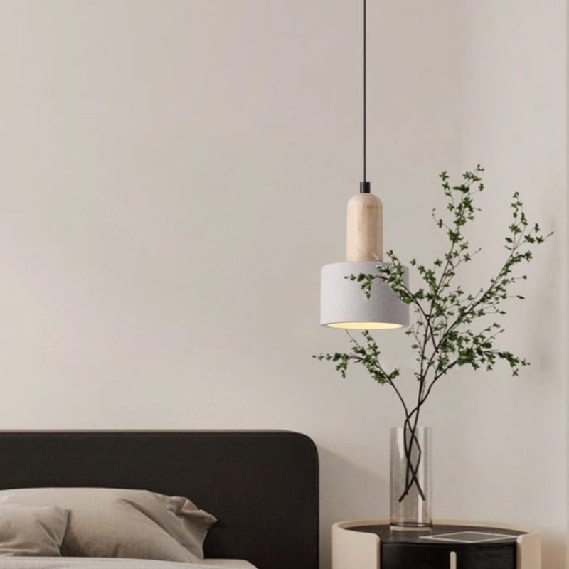 Style B Ozawa cylindrical pendant beside a bed and a vase of leafy branches.