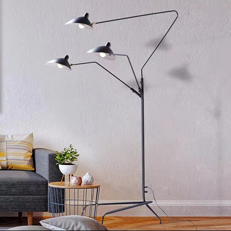 Black three-head floor lamp with visible bulbs beneath cone shades beside a Dark Gray sofa and wire table with a plant