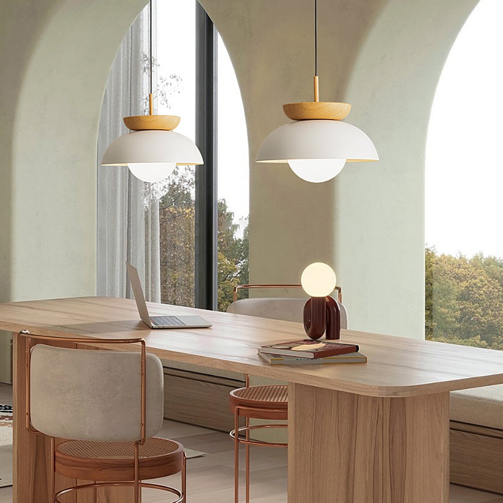 Two lit white dome pendants with wood crowns above a wooden table beside arched windows and a laptop