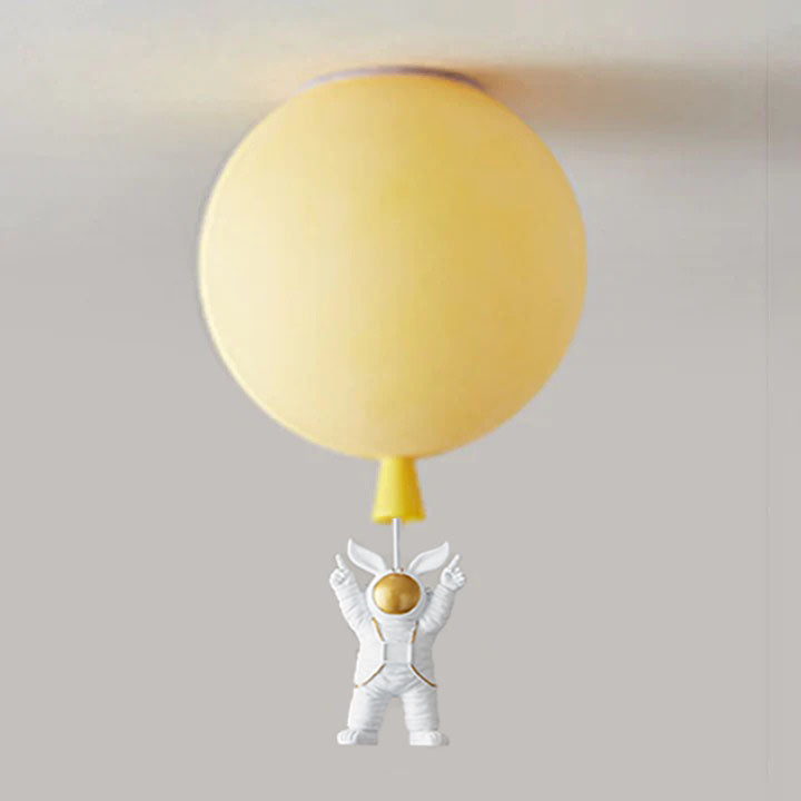 Yellow balloon globe at the ceiling with a both-arms-up white astronaut and gold-tone visor below a fine link.