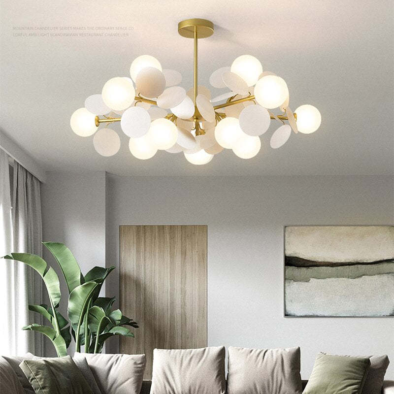 White Jevon globe and petal light above a gray sofa with green cushions, a large plant and a wood door.