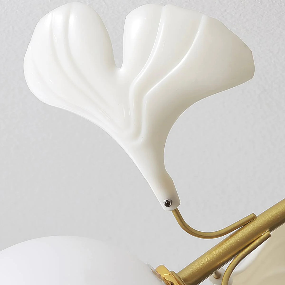 Olivia close-up of a pale veined ginkgo leaf ornament, its screw connection and a curved gold-tone arm above part of a white globe.