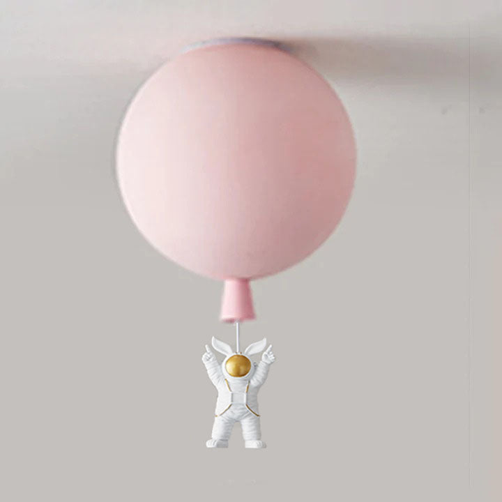 Pale pink balloon globe above a both-arms-up white astronaut with gold-tone visor and pointed helmet-side decoration.
