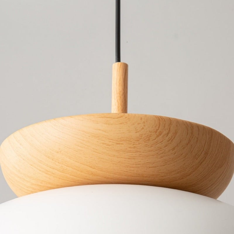 Detail of the grain-patterned wood crown and sleeve where the black pendant cord enters, above part of a white dome