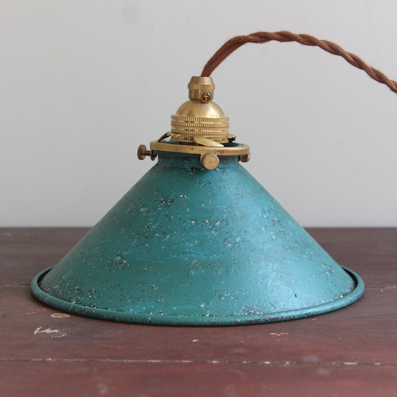 Blue cone shade and gold-tone fitting resting on a dark wood table beside a twisted brown cord