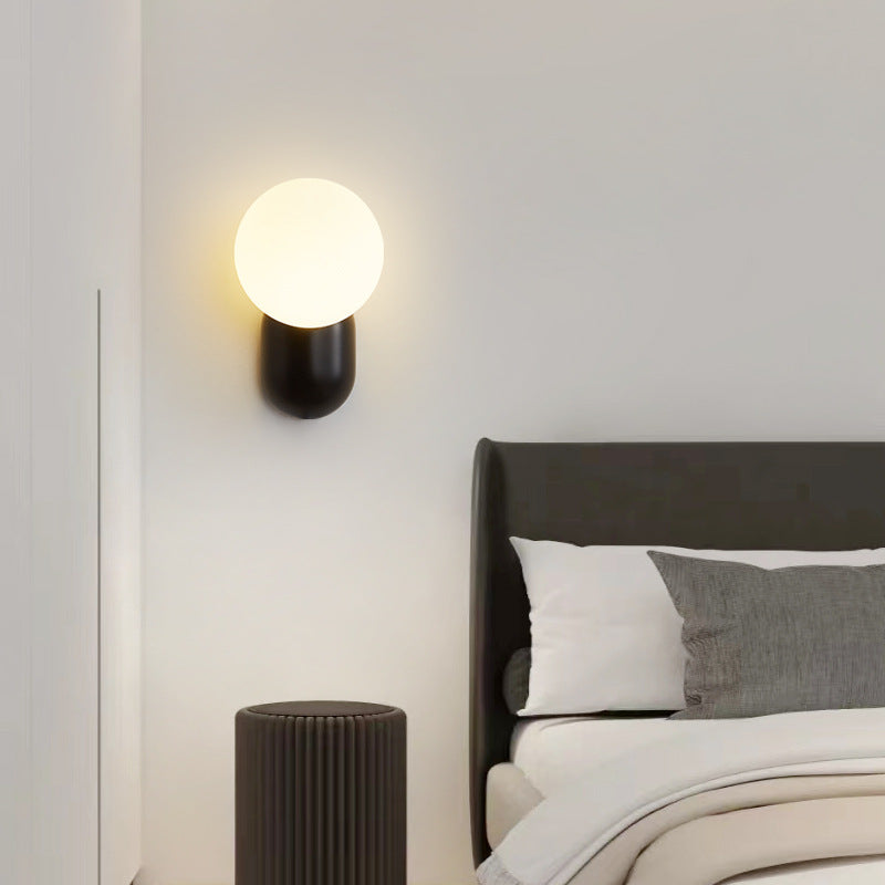 Black Hailie glass globe wall lamp beside a bed