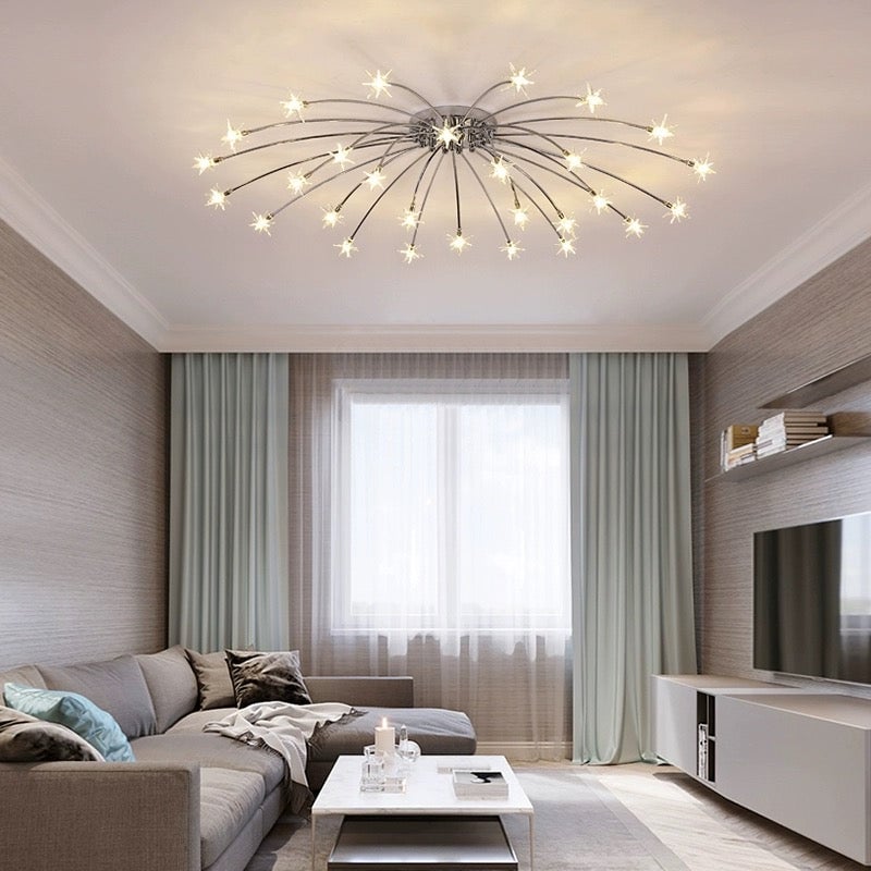 Chrome-tone wide starburst ceiling light above grey sectional sofa, white coffee table and window with pale green curtains