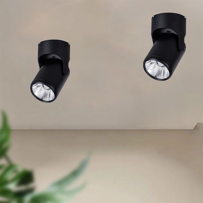 Two black Novak ceiling spotlights with tilted heads above blurred greenery