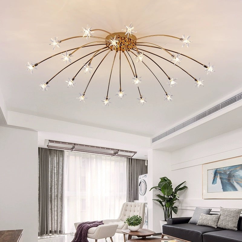 Gold-tone radial ceiling lamp with clear stars over bright living room with black sofa, cream chair and green plant