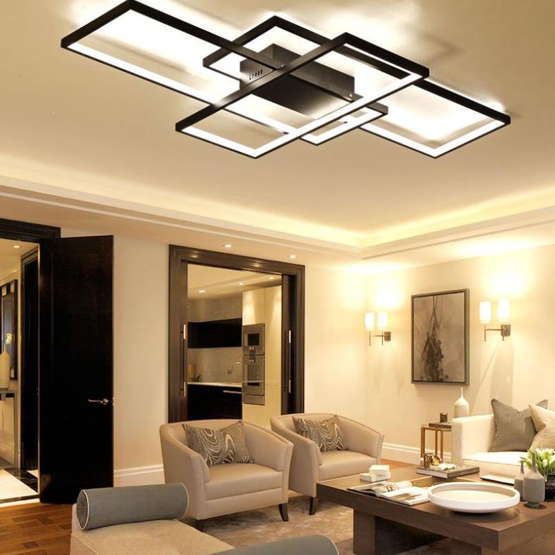Black rectangular-frame ceiling light with warm-looking illumination above beige armchairs, a coffee table and wall sconces
