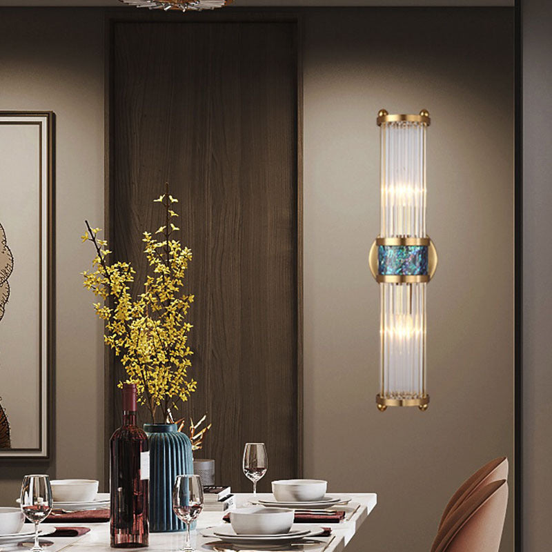 Gold-tone wall light beside a dining table with wine bottles, glassware and yellow flowers