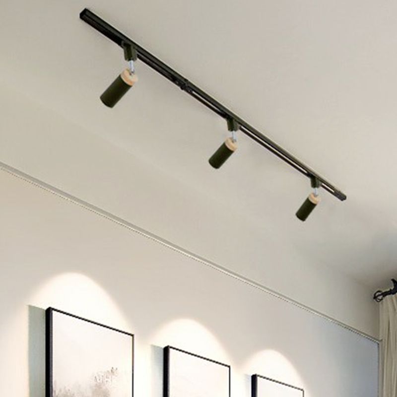 Black three tubular spotlights angled along a ceiling rail above framed pictures and wall light pools